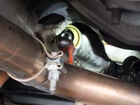 2003 Ford Crown Victoria - Yellow seal collar at the transmission output sits behind an exhaust pipe joint and U-bolt clamp in close view.
