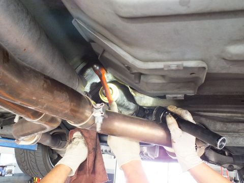 2003 Ford Crown Victoria - Gloved hands guide a driveshaft into place between exhaust pipes beneath a lifted car; shop floor below.