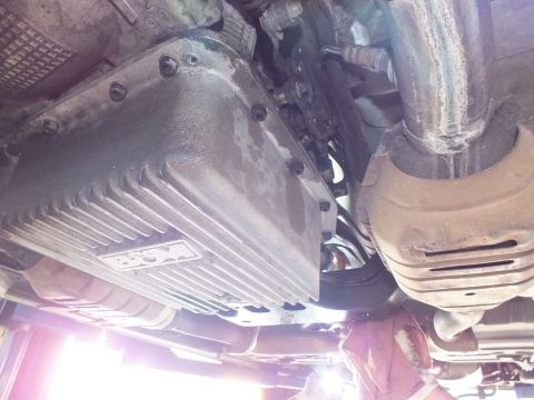 2003 Ford Crown Victoria - ribbed transmission oil pan sits beside an exhaust pipe and heat shield in an underbody view of a raised car.