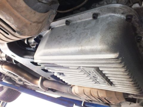 2003 Ford Crown Victoria - Deep-finned cast transmission pan with raised emblem mounts to the gearbox above an exhaust pipe on the lift.