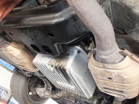2003 Ford Crown Victoria - finned transmission pan and frame rail sit beside an exhaust downpipe; a tire shows at the lower left.