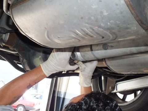 2003 Ford Crown Victoria - Gloved hand guides an exhaust pipe into the muffler heat shield while the car sits on a lift.