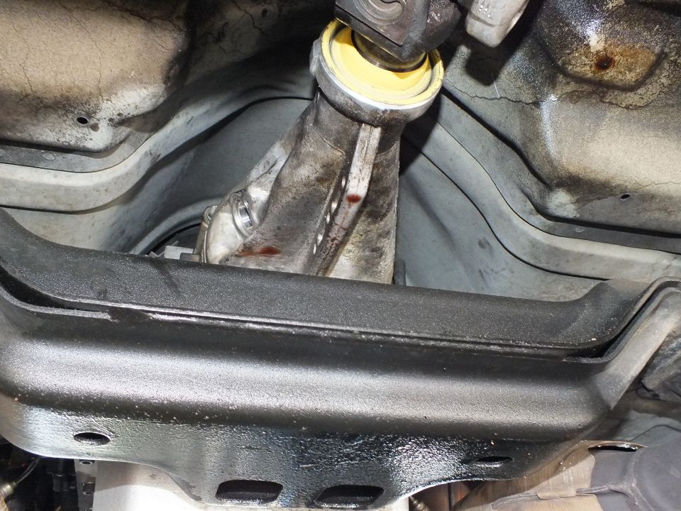 Driveshaft with yellow support bearing above a black crossmember and ribbed transmission pan