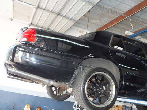 2003 Ford Crown Victoria - Rear quarter of the black Crown Victoria on the lift, wearing a Supermotors window decal.
