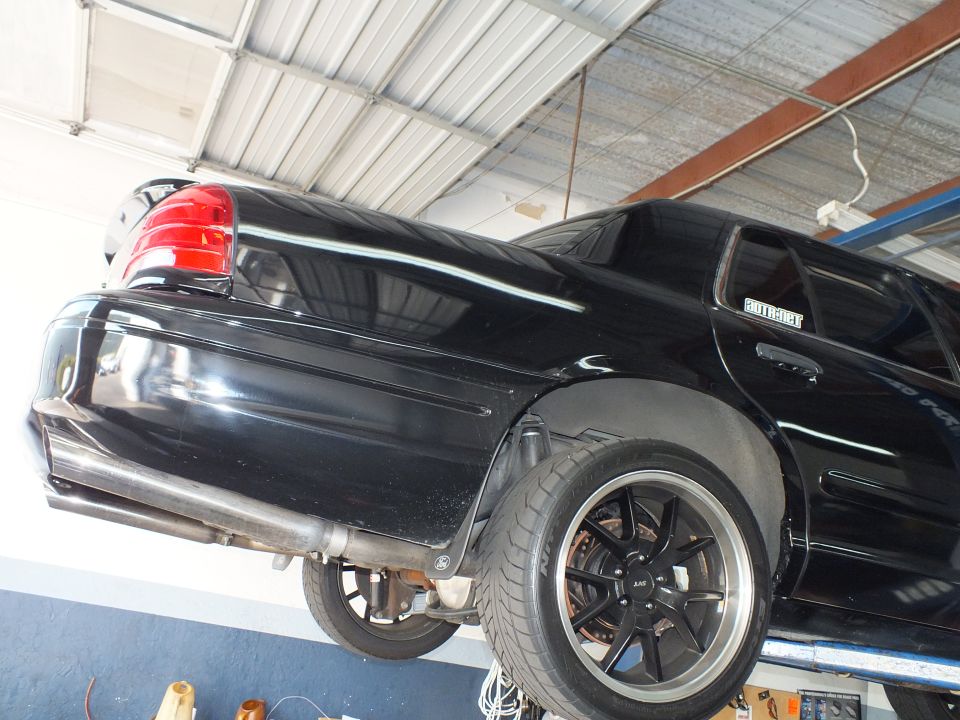 Black Ford Crown Victoria rear quarter on a lift with Supermotors decal and black wheel