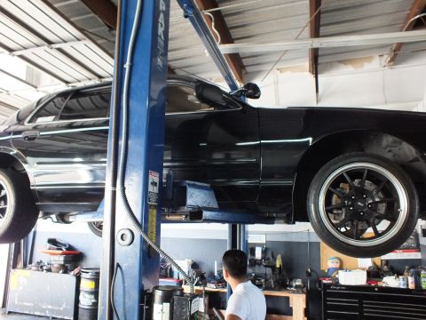 2003 Ford Crown Victoria - Technician works beneath the black sedan raised on a blue two-post lift in the shop.