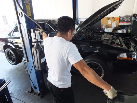 2003 Ford Crown Victoria - Technician reaching into the engine bay of a black sedan raised on a shop lift, hood open.