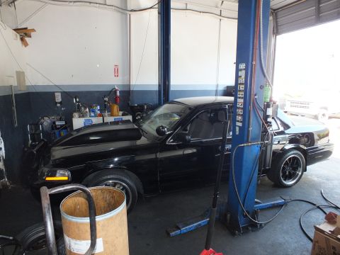 2003 Ford Crown Victoria - Side view of a black four-door sedan staged next to a hydraulic lift in a service bay.