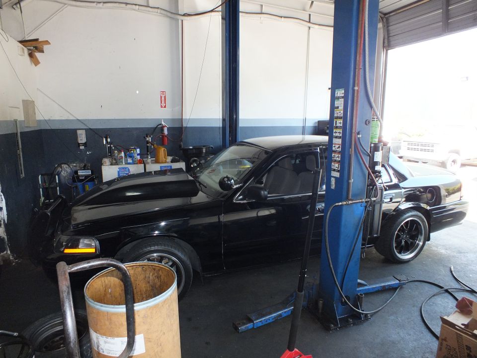 Black Ford sedan parked beside a blue two-post lift inside an automotive repair shop