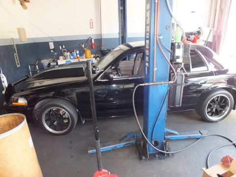 2003 Ford Crown Victoria - Profile of a lowered black sedan with dark wheels staged by a two-post lift in a repair shop.