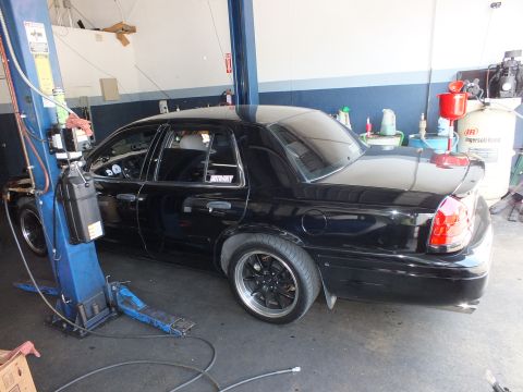 2003 Ford Crown Victoria - Black four-door sedan raised on a lift, rear quarter showing an Interceptor decal and black wheels.