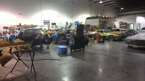1973 Chevrolet Camaro - Multiple vehicles are undergoing repair in a workshop environment, with tools and parts visible around them.