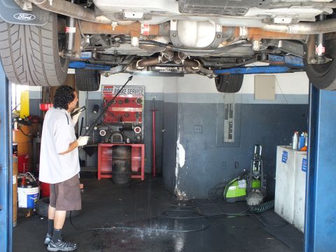 2003 Ford Crown Victoria - Undercarriage view of a lifted vehicle with Ford mud flap and exhaust piping as a worker cleans it.