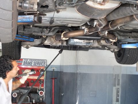 2003 Ford Crown Victoria - Close underbody view of exhaust pipes and transmission with an Ammco brake service banner behind.