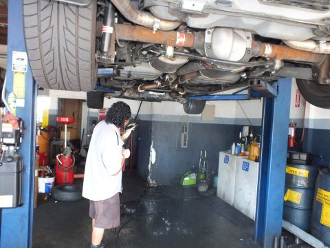 2003 Ford Crown Victoria - Technician examining the exhaust and suspension under a hoisted vehicle in a garage.