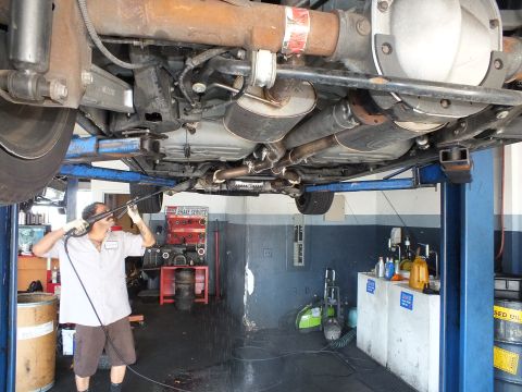 2003 Ford Crown Victoria - Underbody view of rear axle and exhaust while a mechanic pressure-washes beneath a hoisted vehicle.