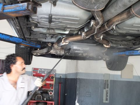 2003 Ford Crown Victoria - Undercarriage showing dual exhaust and muffler, Ford lift pad, as a worker cleans beneath.