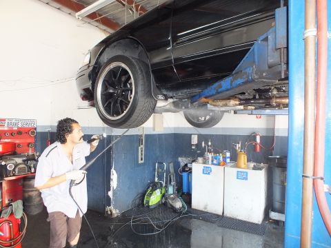 2003 Ford Crown Victoria - Mechanic rinsing the underside of a black sedan raised on a two-post hoist.