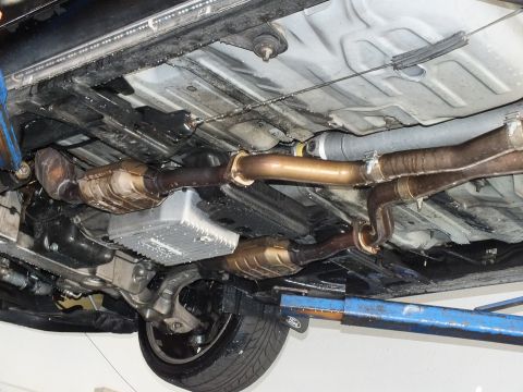2003 Ford Crown Victoria - Underbody view of dual exhaust and catalytic converters with the rear tire and lift pad visible.