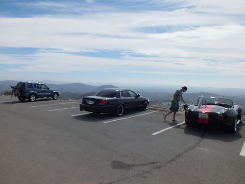 2003 Ford Crown Victoria - Several vehicles including a black sedan and an open-top roadster in a scenic hilltop parking lot.