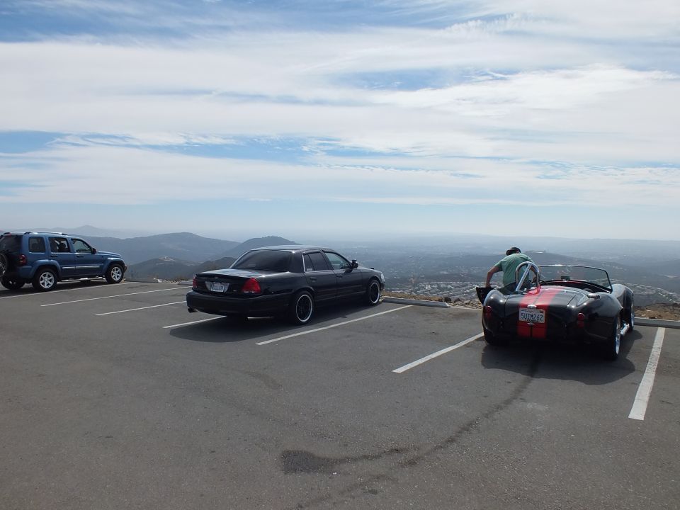 Black sedan and red roadster parked at a mountaintop overlook with a person bent over the roadster