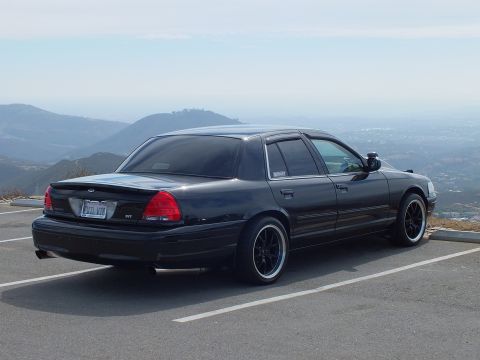2003 Ford Crown Victoria - Black Ford four-door sedan with SVT badging photographed at a hilltop overlook on dark wheels.
