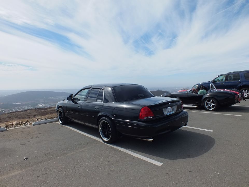 Black Ford sedan parked rear-quarter at a scenic overlook with an SUV and roadster nearby
