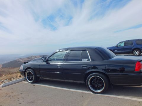 2003 Ford Crown Victoria - Profile of a lowered black four-door sedan with a window decal parked next to an SUV at a hilltop lot.