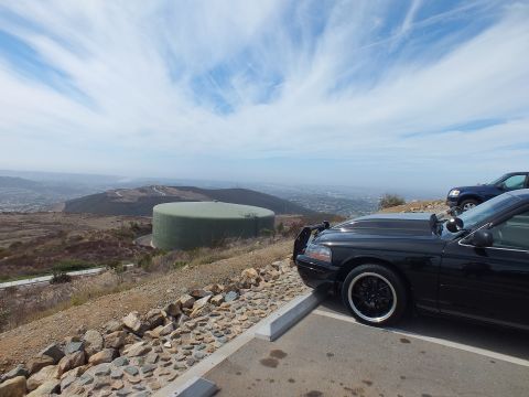 2003 Ford Crown Victoria - Front corner of a lowered black sedan parked above a valley with a green storage tank below.