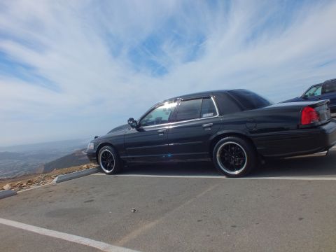 2003 Ford Crown Victoria - Side view of a black four-door sedan lowered on dark wheels above a hazy valley.