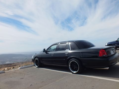 2003 Ford Crown Victoria - Rear quarter of a black four-door sedan parked overlooking distant hills.