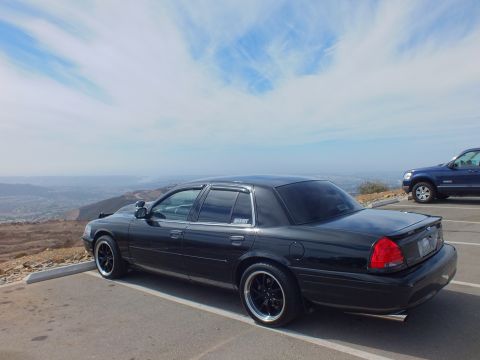 2003 Ford Crown Victoria - Lowered black sedan shown from the rear in a paved overlook with an SUV alongside.