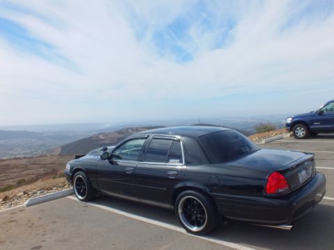 2003 Ford Crown Victoria - Black sedan with chrome window trim parked at a mountaintop overlook lot.