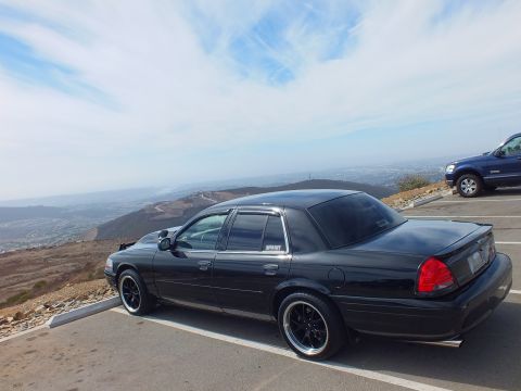 2003 Ford Crown Victoria - Side-rear view of a black four-door above a valley, blue SUV parked nearby.