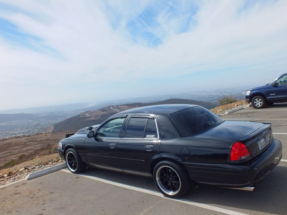 Black Crown Victoria sedan rear profile lowered on dark rims at scenic overlook