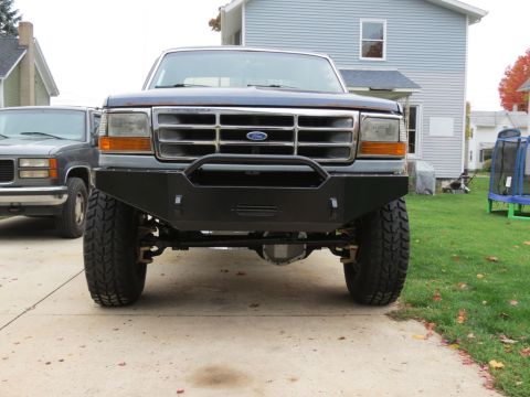 1989 Ford Bronco - Front view of a dark blue Ford Bronco with an aftermarket bumper and large tires, parked in a driveway.