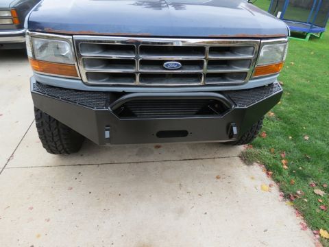 1989 Ford Bronco - Front view of a blue Ford truck a black winch-ready bumper and chrome grille.