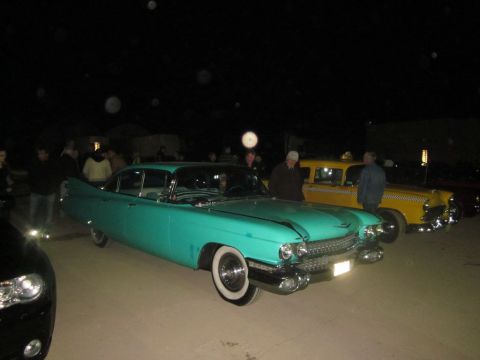 1991 Ford LTD Crown Victoria - A turquoise classic car and a yellow taxi are parked side-by-side at an outdoor gathering at night.