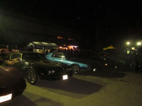 1991 Ford LTD Crown Victoria - A gathering of cars at night, with people and tents visible in the background.