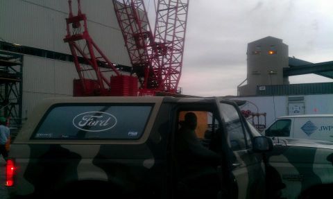 1995 Ford Bronco - A Ford Bronco with a camouflage paint job is parked near industrial equipment and a crane.