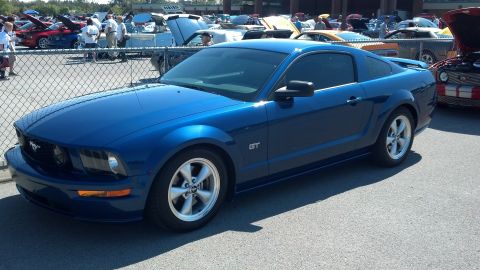 2007 Ford Mustang - A blue 2007 Ford Mustang GT is parked at an outdoor car show, with other vehicles and people in the background.