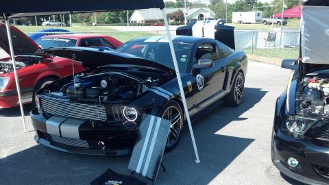 2007 Ford Mustang - A black 2007 Ford Mustang with silver racing stripes is displayed at a car show, with its hood open to reveal the engine.