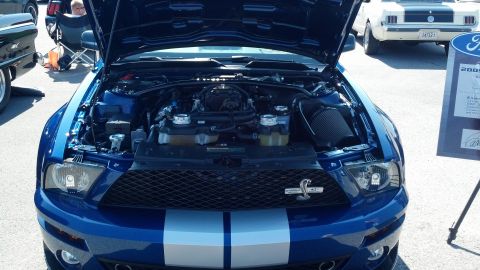 2007 Ford Mustang - A blue 2007 Ford Mustang GT500 is displayed with its hood open, revealing the engine bay. Another classic Mustang is visible in the backgro…