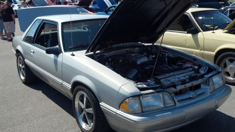 2007 Ford Mustang - A silver Ford Mustang from the late 1980s is displayed with its hood open at an outdoor car show.