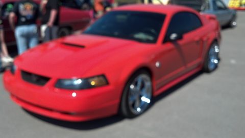 2007 Ford Mustang - A red Ford Mustang is parked outdoors, with people and other vehicles blurred in the background.