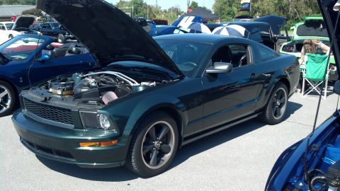 2007 Ford Mustang - A dark green 2007 Ford Mustang coupe is displayed with its hood open at a car show event.
