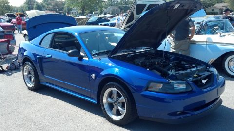 2007 Ford Mustang - A blue coupe is displayed with its hood open at an outdoor car show, next to a vintage two-tone car.