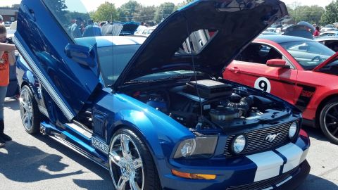 2007 Ford Mustang - A blue 2007 Ford Mustang with custom lambo doors and racing stripes is displayed at a car show.