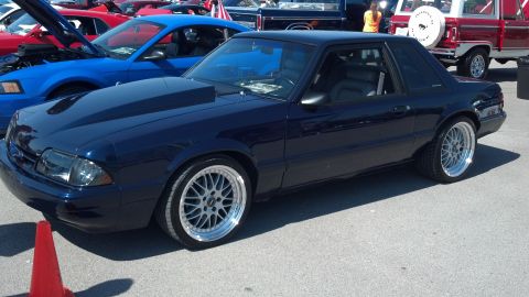 2007 Ford Mustang - A dark blue Ford Mustang coupe with a prominent hood scoop and custom wheels is parked at a car show.