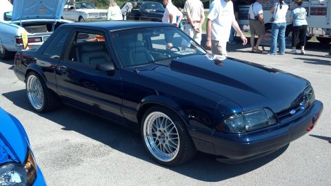 2007 Ford Mustang - A dark blue coupe with a prominent hood scoop and custom wheels is displayed at an outdoor event.